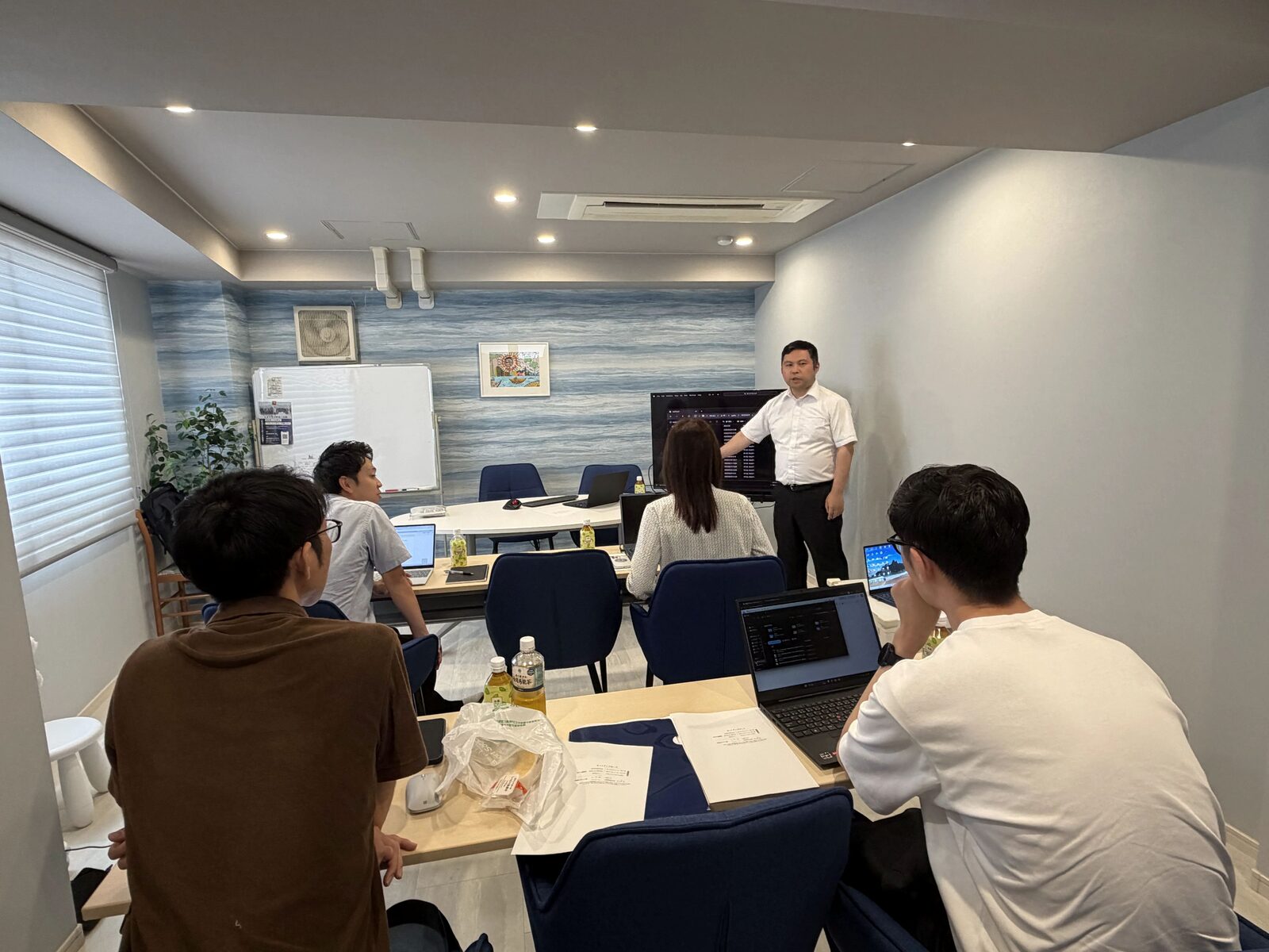会議室で、正面に立つ伊藤の説明を聞きながら、参加者がそれぞれのノートPCで作業している様子